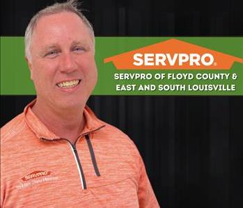 Man wearing a grey shirt standing against a green wall with SERVPRO sign