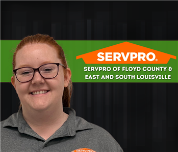 red haired woman smiling at camera with a dark background and a servpro logo on the wall