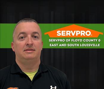 man looking at the camera wearing a servpro shirt with a dark background behind him and a servpro logo on the wall